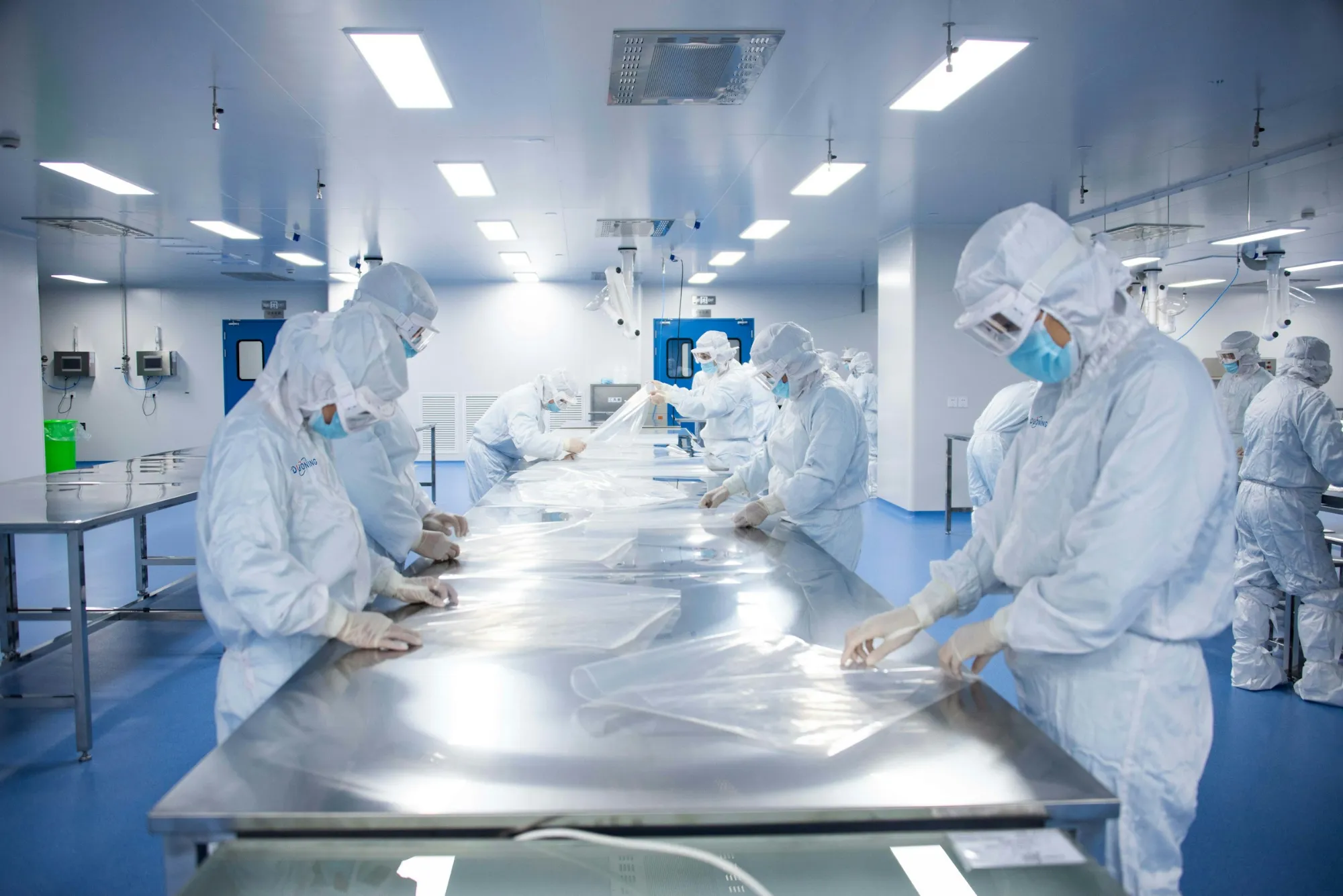 A cleanroom where gowned operators work at stainless steel tables