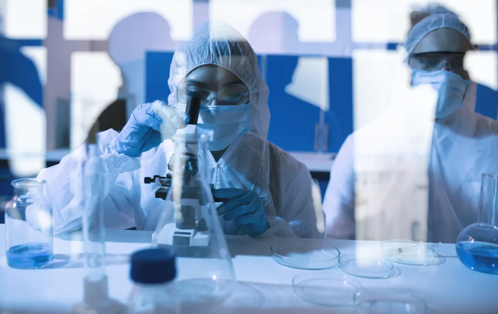 Two scientists in cleanroom gowning, at a microscope