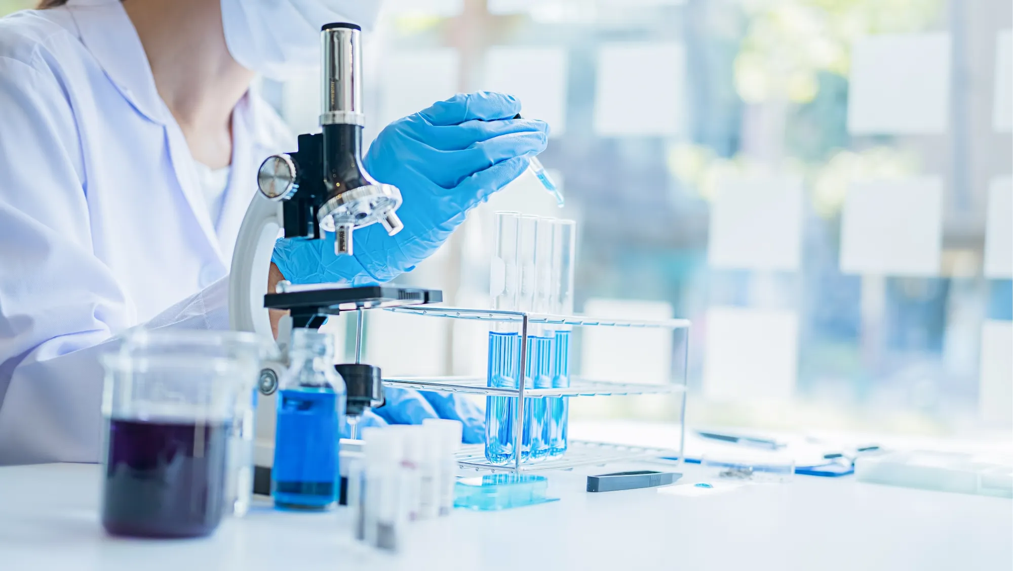 Microscope, blue tubes and gloved hands in a bright laboratory