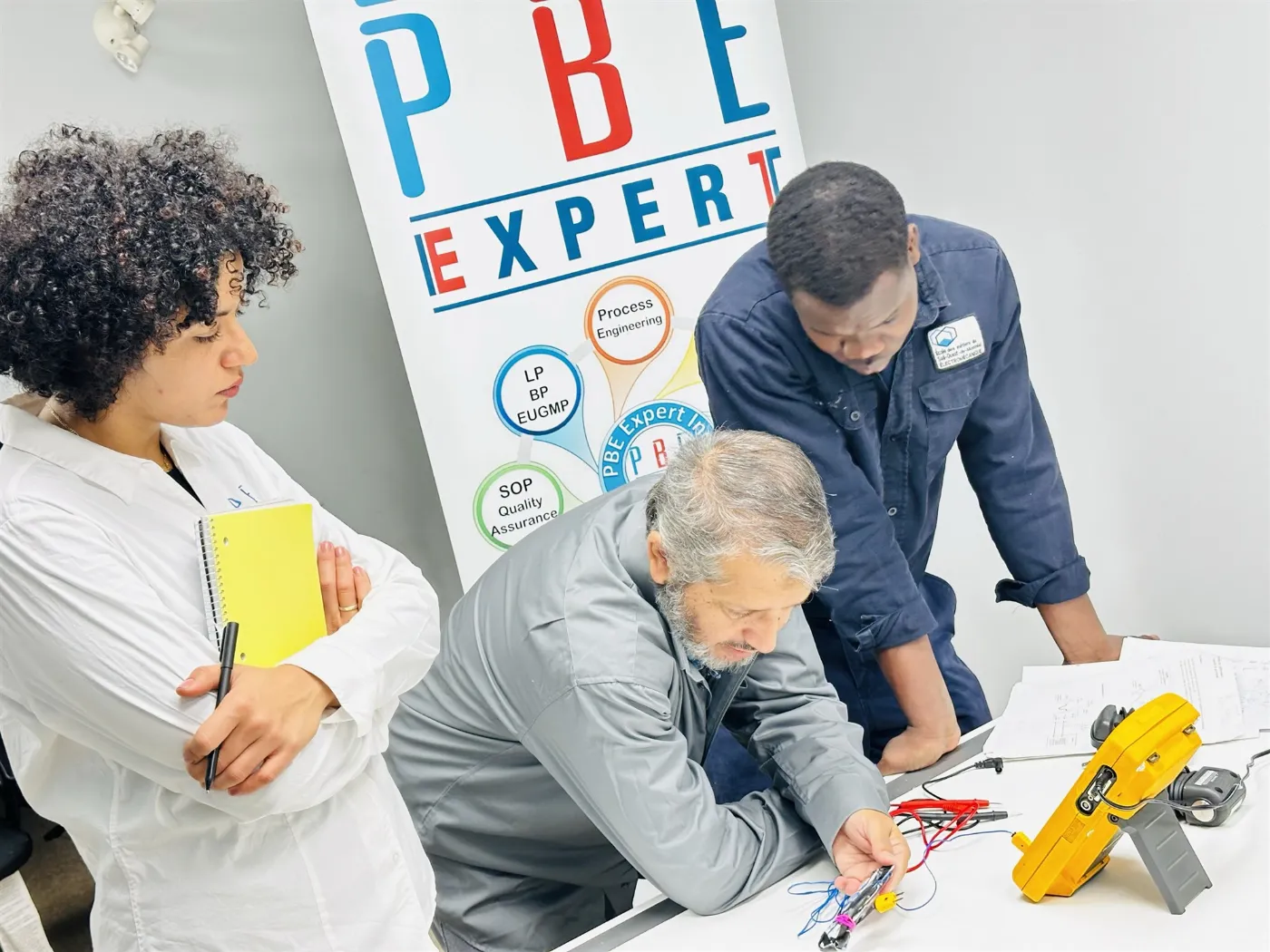 Des membres de l’équipe de PBE Expert penchés sur un montage électrique, devant la bannière de l’entreprise