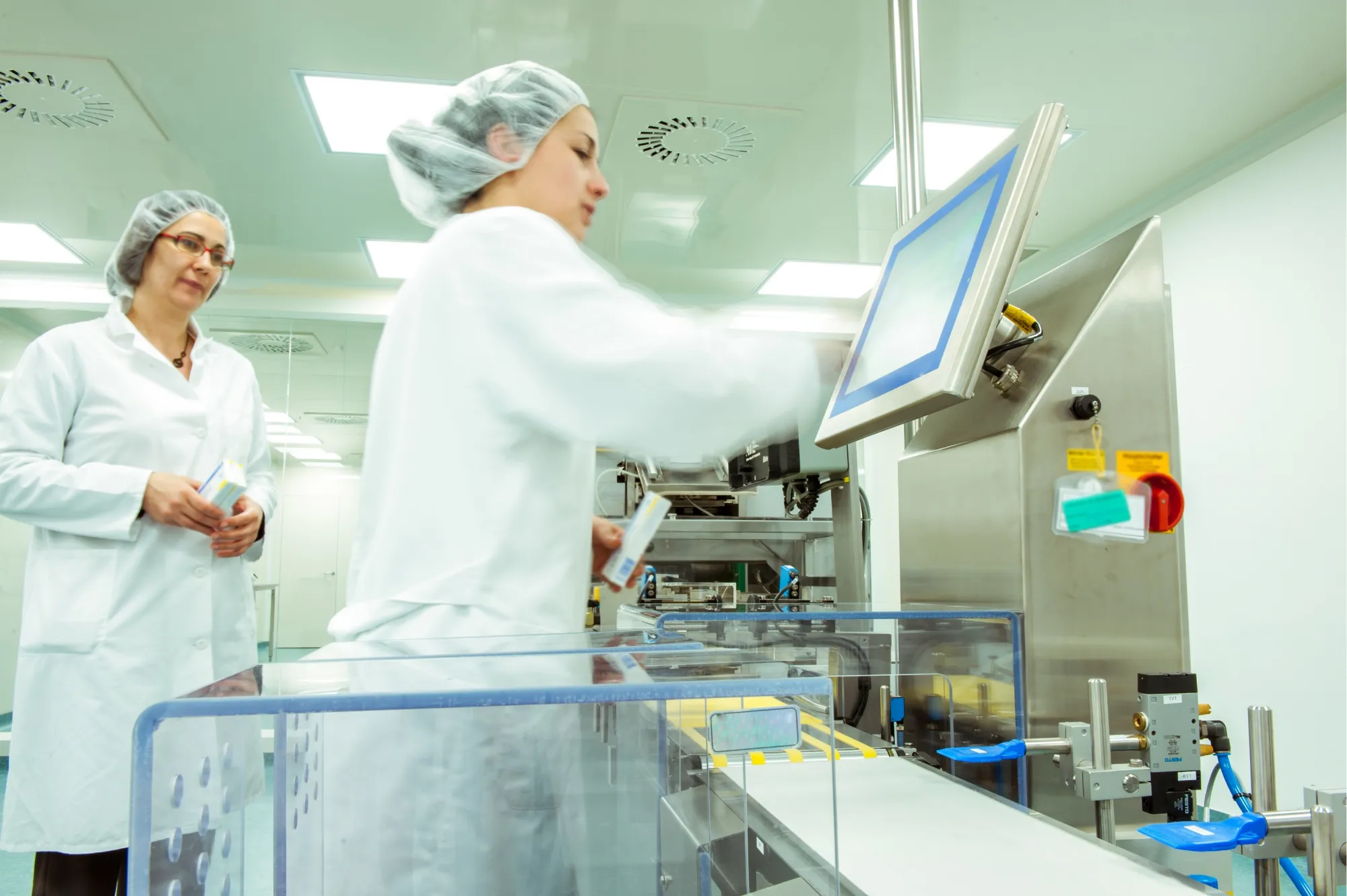 A trainer guides a technician at her workstation on a cleanroom production line