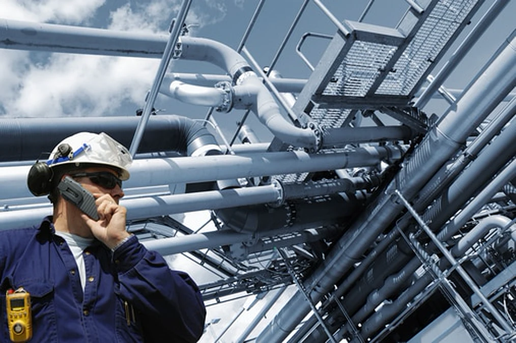 Engineer in a hard hat coordinating by radio, surrounded by plant piping