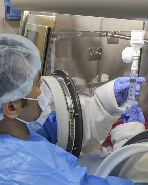 Sterile compounding in a glove isolator, wearing a gown, bouffant cap, mask and gloves